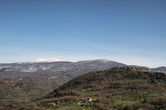 talian Countryside. Tuscany. Daylight. Blue Sky. Spring. Green Hills, a Peaceful Village, a Snowy Mountain in the Background