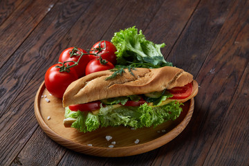 Fresh sandwich with lettuce, tomatoes and cheese served on wooden plate over wooden background, selective focus