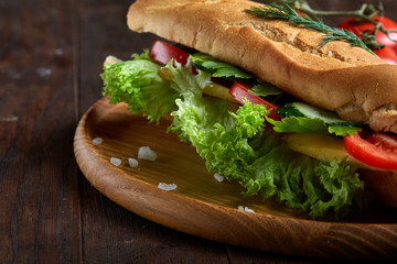 Fresh sandwich with lettuce, tomatoes and cheese served on wooden plate over wooden background, selective focus