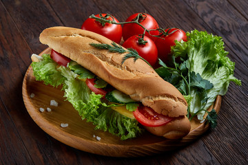 Fresh sandwich with lettuce, tomatoes and cheese served on wooden plate over wooden background, selective focus