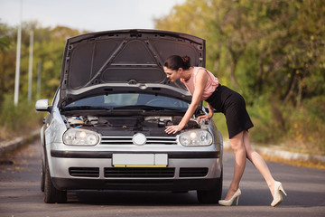 Fototapeta na wymiar Young woman looks under the hood of her car and trying to find the cause of breakage