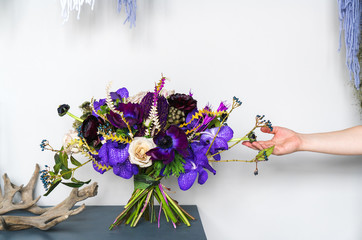 violet wedding bouquet stands on a table in the interior with the hands of a female florist. Wedding trends in color.