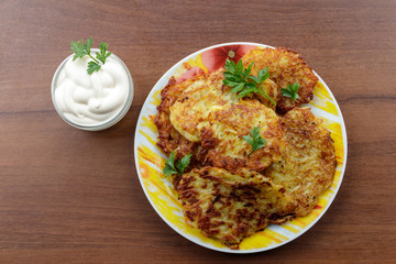 Homemade fried potato pancakes with sour cream on wooden table