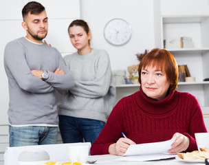 Obraz premium Upset elderly mother with documents, dissatisfied children behind