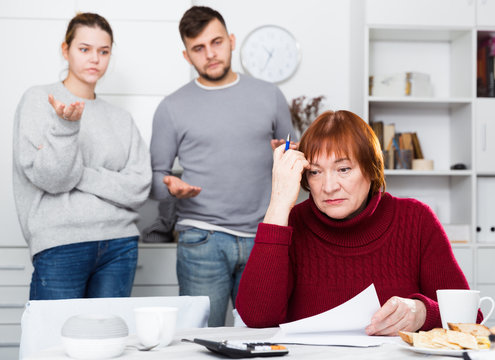Distressed aged woman with paperwork and irritated family behind