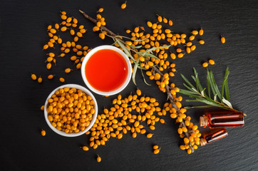 Plakat Sea buckthorn with bottle and bowl with sea buckthorn oil isolated on black stone table. Top view.