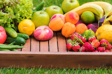 Various vegetables and fruits on a wooden tray against a background of green grass