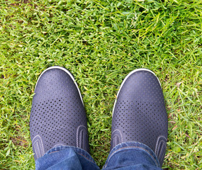 A man in jeans and summer shoes on the background of green grass . Loafers.