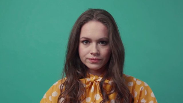 Curly young woman covers her head with her hands and shakes it on a freen background. Disagreement, pain, argue. Negative emotions, bad mood. Slow motion, close up view, female portrait