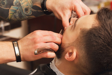 Barber shaving a bearded man in a barber shop, close-up