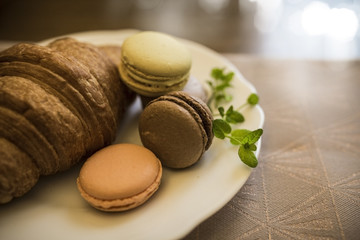 Plate with freshly baked delicious croissant and colored macaroon