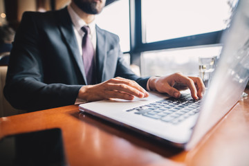 Close up focus view of young businessman in suit typing on a laptop keyboard at the cafe.