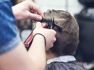 Fototapeta premium Hairdresser making a haircut to a boy with clipper.