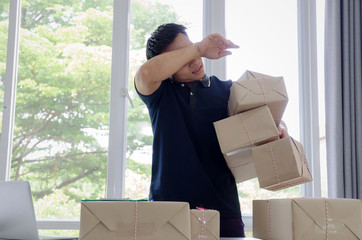 tired handsome young asian delivery man wiping sweat and lifting many packaging parcel box in home...