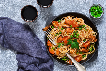 Pasta with tomatoes, green peas and mussels in a cast-iron frying pan on a concrete background.