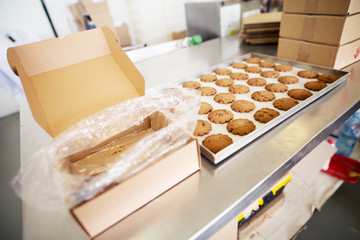Warm freshly baked cookies cooling on a desk inside of food production factory before being packed in a brown box.