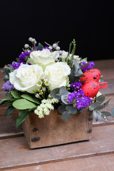 Festive flower arrangement of white roses, white and blue kermek and other plants, red eggs for Easter decorated on wooden and black background.