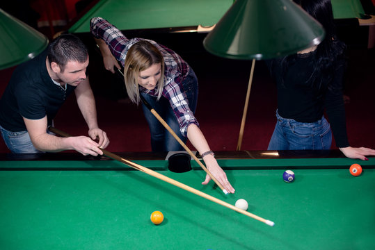 Blond girl is learning how to play billiard