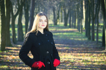 Young beautiful girl in a black coat red gloves exploring spring forest smoke park.