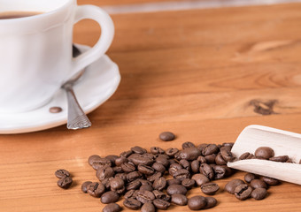 Mug, dispenser with coffee, wooden spoon and a scattering of coffee beans on a wooden background