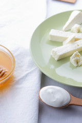 Cheese, honey and sour cream, feta in green plate, soft cheese on white background, wooden spoon with sour cream, French breakfast, blue napkin, honey in glass dishes, copy space, blurred background