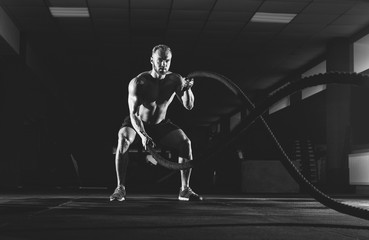 Athletic young man with battle rope doing exercise in the fitness gym. Sports concept.