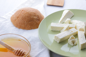 Cheese, honey and sour cream, a piece of bread, feta in a green plate, soft cheese on a white background, a wooden spoon with sour cream, French breakfast, blue napkin, honey in glassware, art