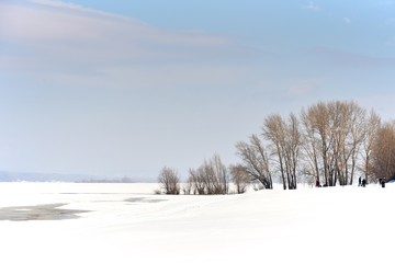 Trees on the shallows of a frozen river. Winter sunny day. Ice and snow.
