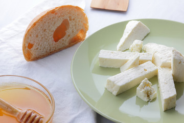 Cheese, honey and sour cream, a piece of bread, feta in a green plate, soft cheese on a white background, a wooden spoon with sour cream, French breakfast, blue napkin, honey in glassware, art