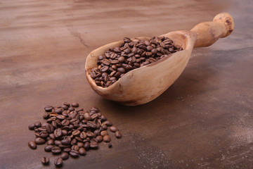 coffee beans in a wooden scoop on dark stone table.