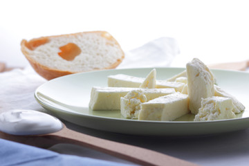 Cheese, honey and sour cream, a piece of bread, feta in a green plate, soft cheese on a white background, a wooden spoon with sour cream, French breakfast, blue napkin, honey in glassware, art