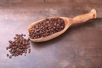 coffee beans in a wooden scoop on dark stone table.