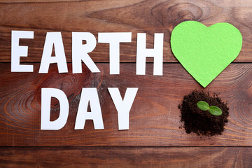 Inscription Earth Day with young plant in ground on wooden table