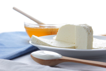 Cheese, honey and sour cream, feta in a white plate, soft cheese on a white background, wooden spoon with sour cream, French breakfast, blue napkin, honey in glassware, blank for designer
