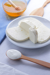 Cheese, honey and sour cream, feta in a white plate, soft cheese on a white background, wooden spoon with sour cream, French breakfast, blue napkin, honey in glassware, blank for designer