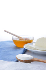 Cheese, honey and sour cream, feta in a white plate, soft cheese on a white background, wooden spoon with sour cream, French breakfast, blue napkin, honey in glassware, blank for designer