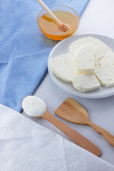Cheese, honey and sour cream, feta in a white plate, soft cheese on a white background, wooden spoon with sour cream, French breakfast, blue napkin, honey in glassware, blank for designer