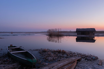 Fototapeta premium beautiful pastel sky just before sunrise over a wild river surrounded by reeds and an ice-covered shore with colorful boats on them