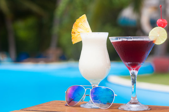 two glasses of fruit cocktails and sunglasses by the pool