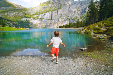 beautiful blue lake oeschinensee, in Switzerland, a fantastic mountain landscape overlooking the water and forest, a small happy baby boy travels and admires nature