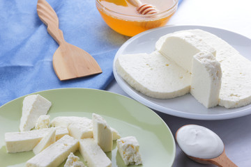 Cheese pattern, honey and sour cream, feta in white and green plate, soft cheese on a white background, wooden spoon with sour cream, French breakfast, blue napkin, honey in glassware
