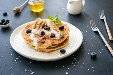 Oat pancakes with greek yogurt, roasted banana, blueberries and cinnamon on white plate