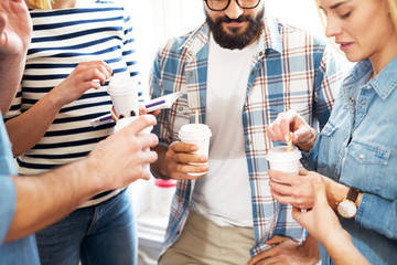 Close up view of young cheerful people having a break and drinking coffee from a paper cups.