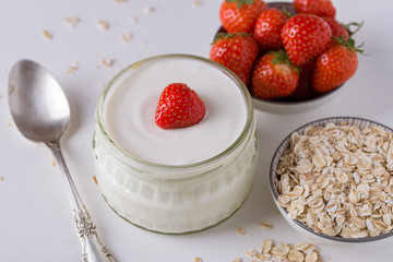 White yogurt in glass bowl with spoon and starwberries on white background.