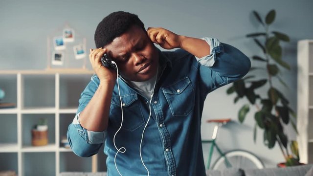 charismatic young african american man with headphones listen music dance in home smile cute face technology musician performance rude style black happy attractive slow motion portrait close up dancer