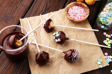 Chocolate cake pops on brown wooden vintage background with colorful sprinkles.