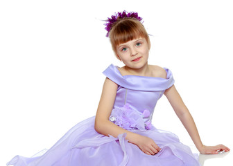 Girl sits on the floor with her hands folded in front of her.