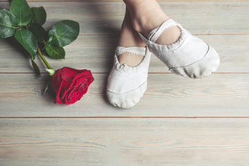 A little dancer and a red rose. Legs of a girl in ballet slippers on a wooden floor © yusev