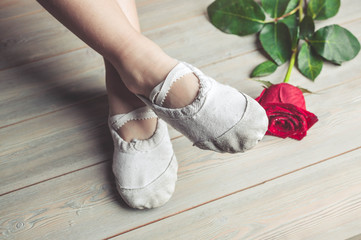 A little dancer and a red rose. Legs of a girl in ballet slippers on a wooden floor © yusev