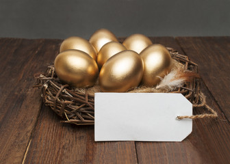 Nest with golden eggs with a tag and place for text on a wooden background. The concept of successful retirement